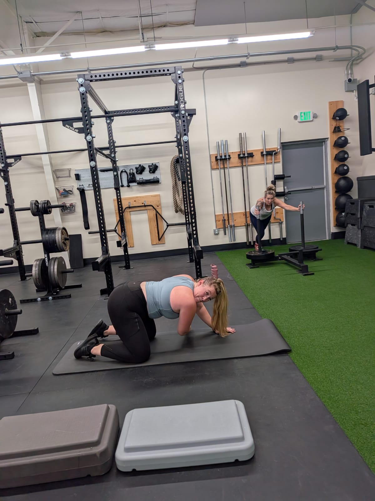 Two women performing different strength exercises during a group training session at Ascent