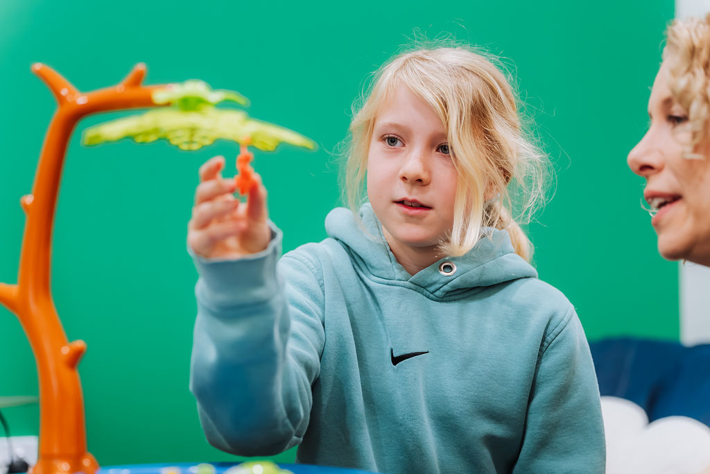 A child holding a game piece while playing a table game with a Totally Psyched clinician