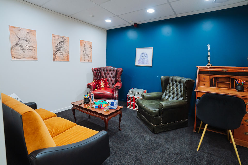 A Totally Psyched therapy room with a deep blue wall, leather wingback chairs and toys on a coffee table