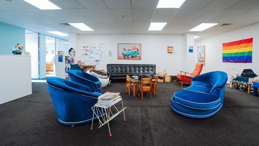 The Totally Psyched waiting area with blue velvet armchairs, a children's table and a rainbow flag