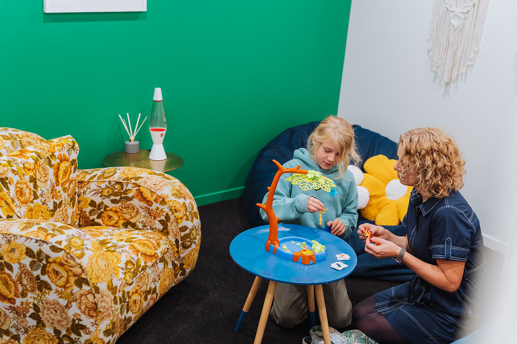 A Totally Psyched clinician and a child playing a table game in a green-walled therapy room