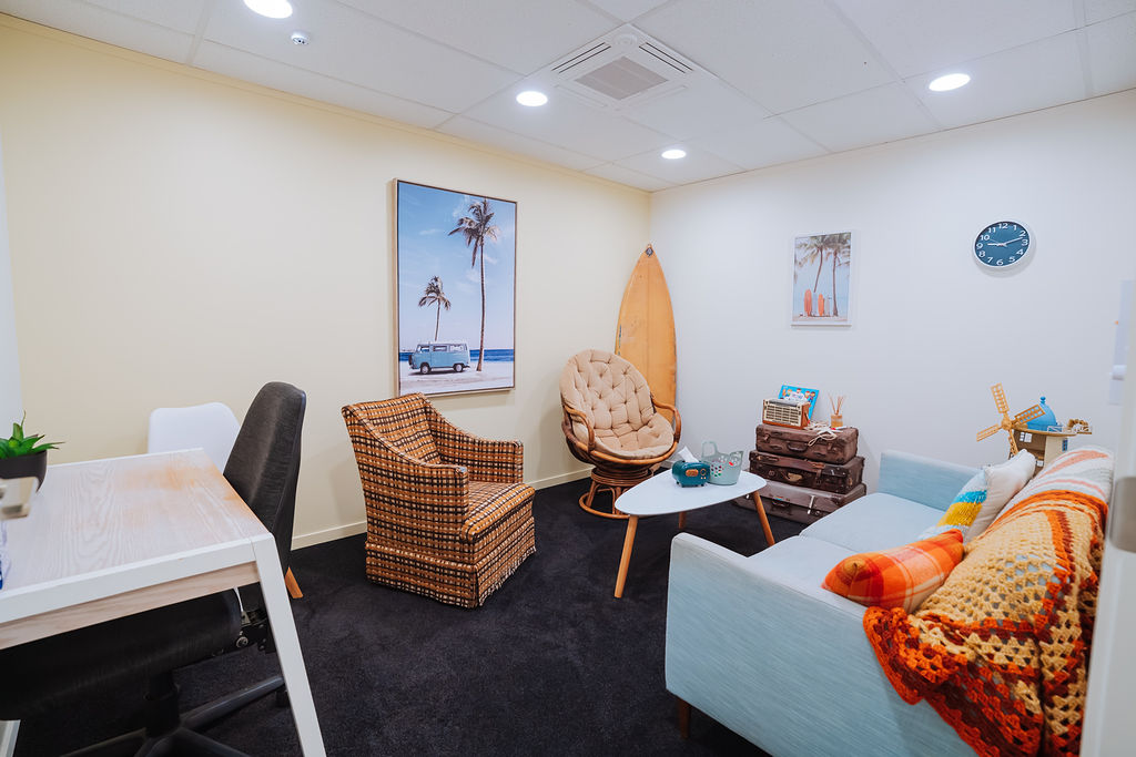 A beach-themed Totally Psyched therapy room with wicker chairs, a surfboard and a pale blue sofa