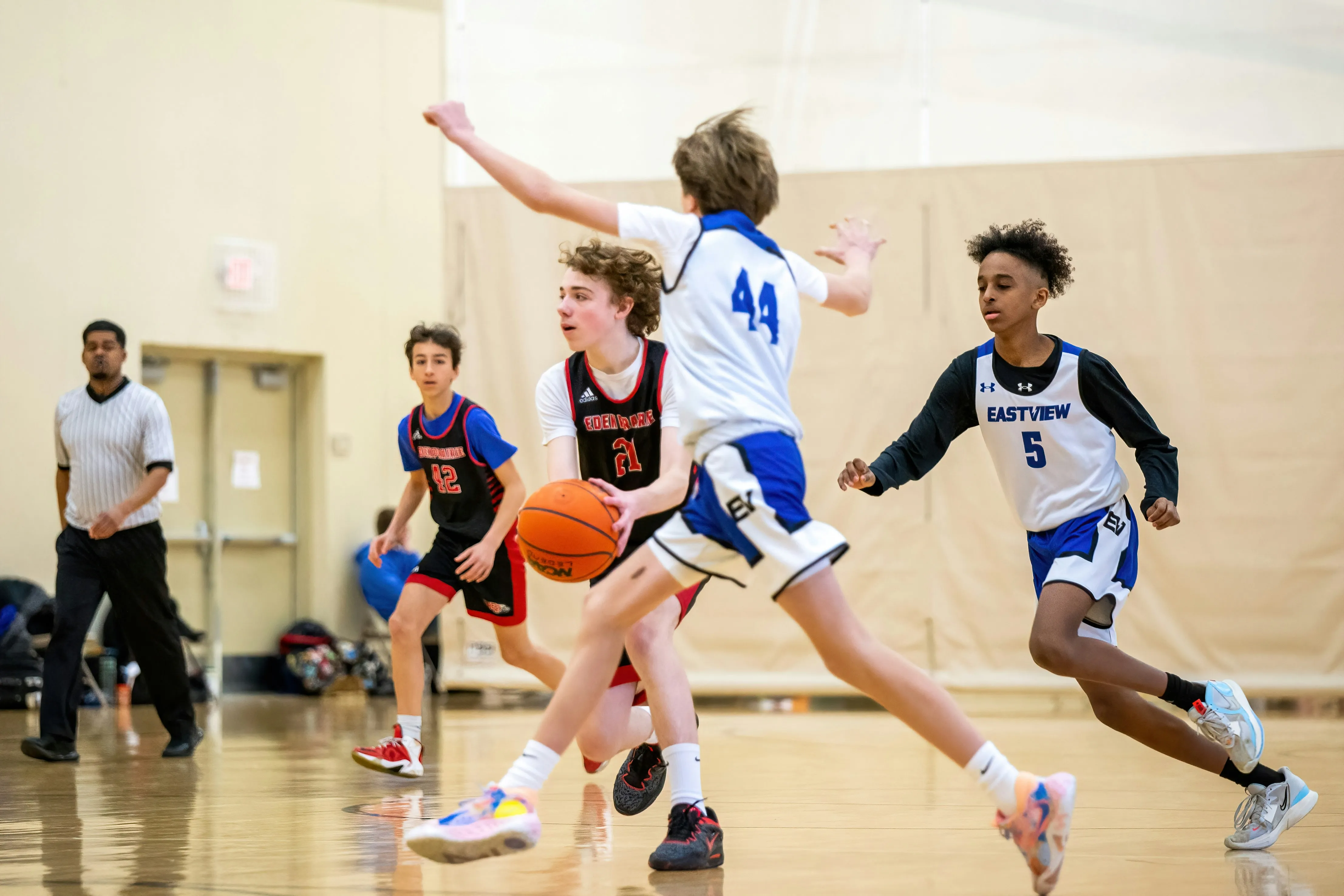 Youth basketball players in action during a game, one player holding the ball and others defending.