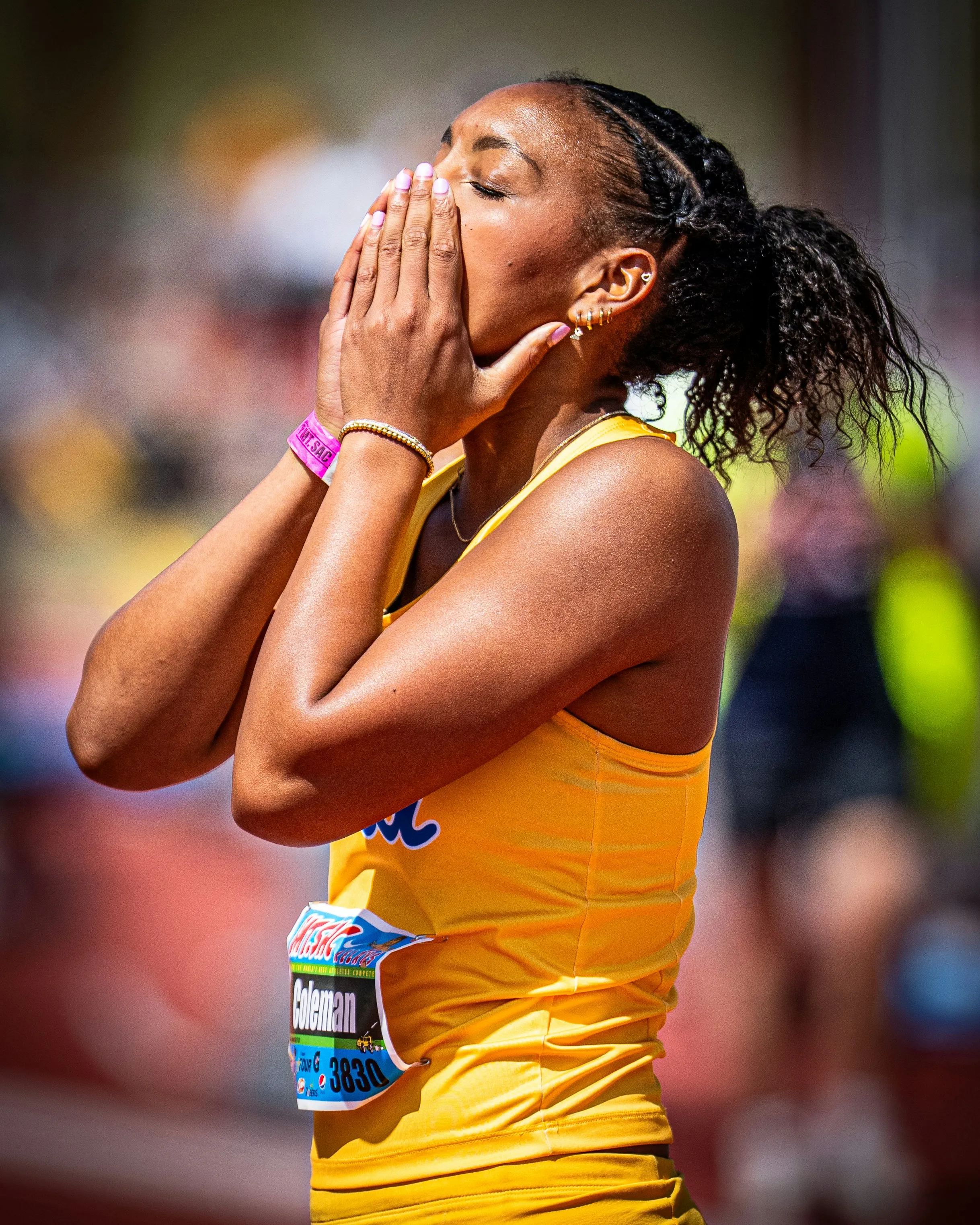 Female athlete in yellow uniform covering her mouth with hands in an outdoor track event.