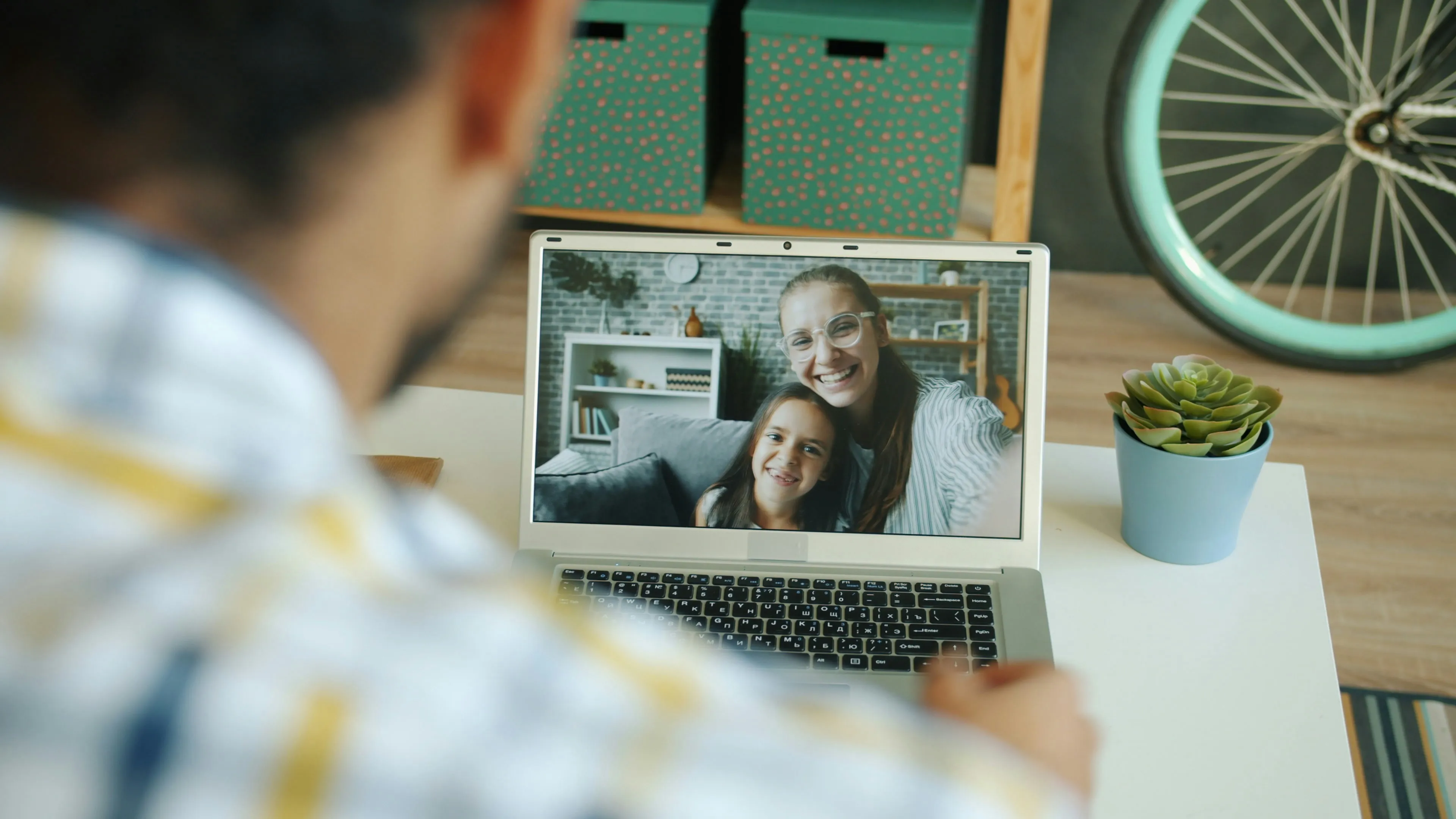 Person video chatting on laptop with smiling woman and child in a cozy living room setting.