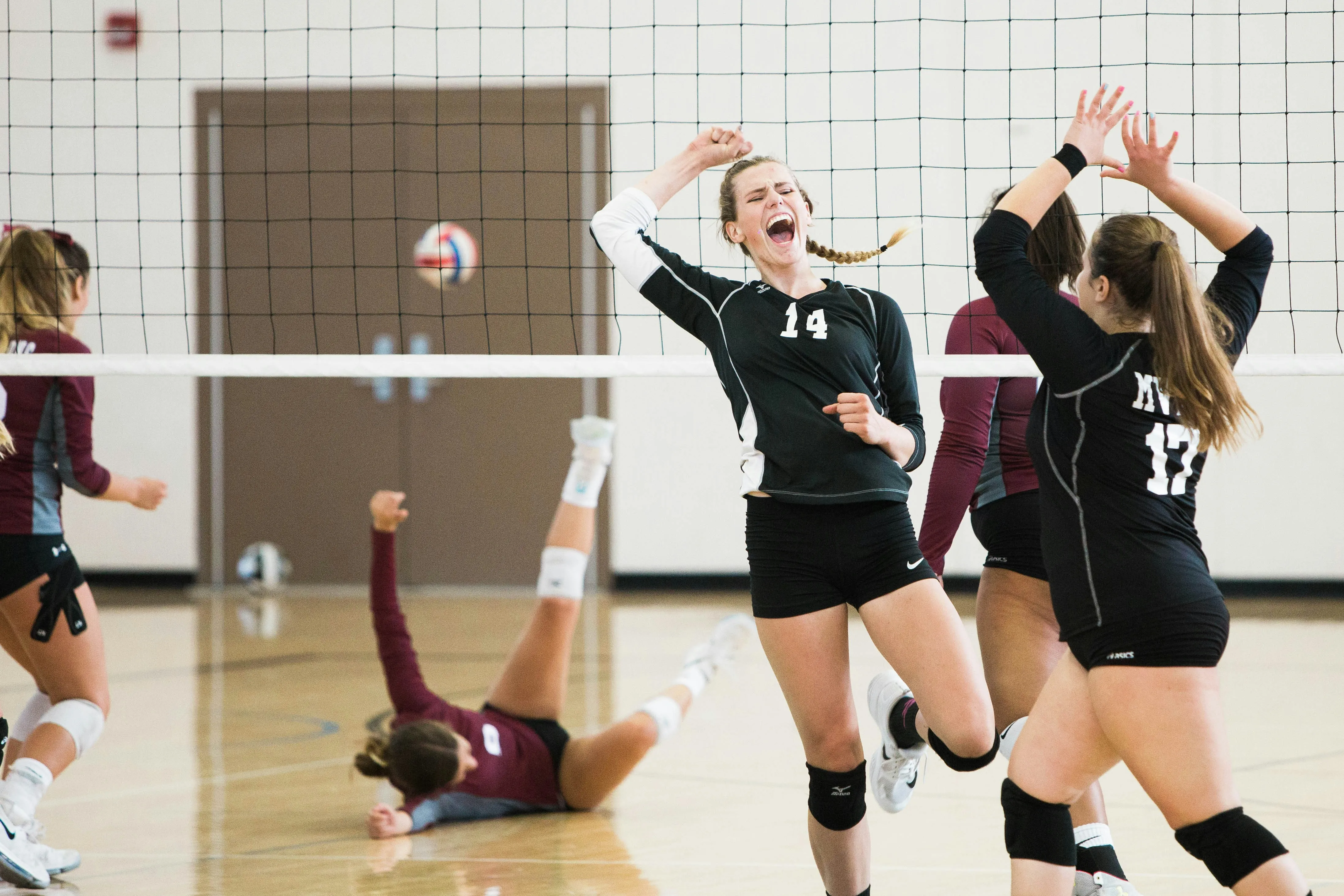 Female volleyball players celebrating a point with excitement during a game in a gym.