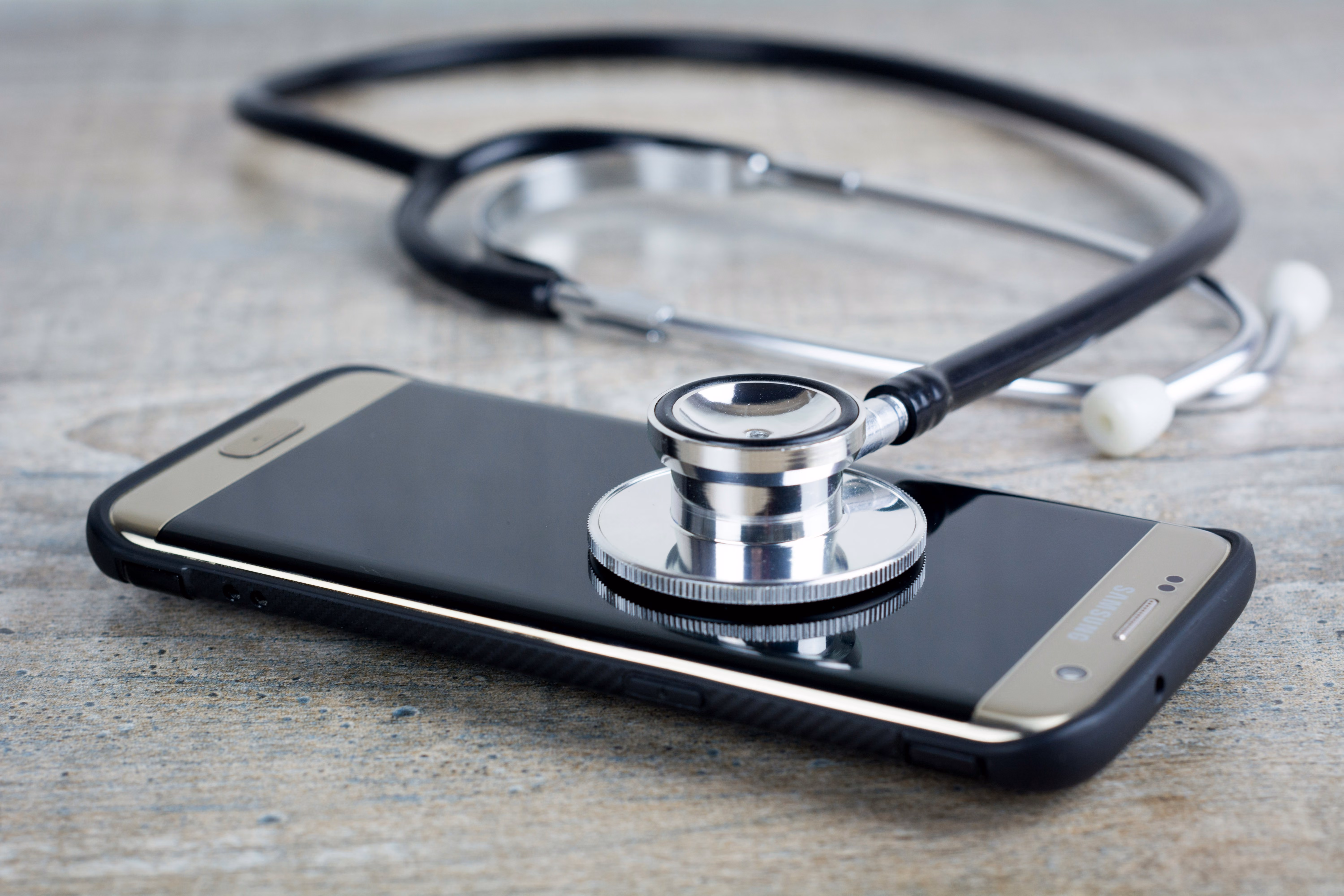 Stethoscope placed on a smartphone on a wooden surface, symbolizing telehealth or digital health care.