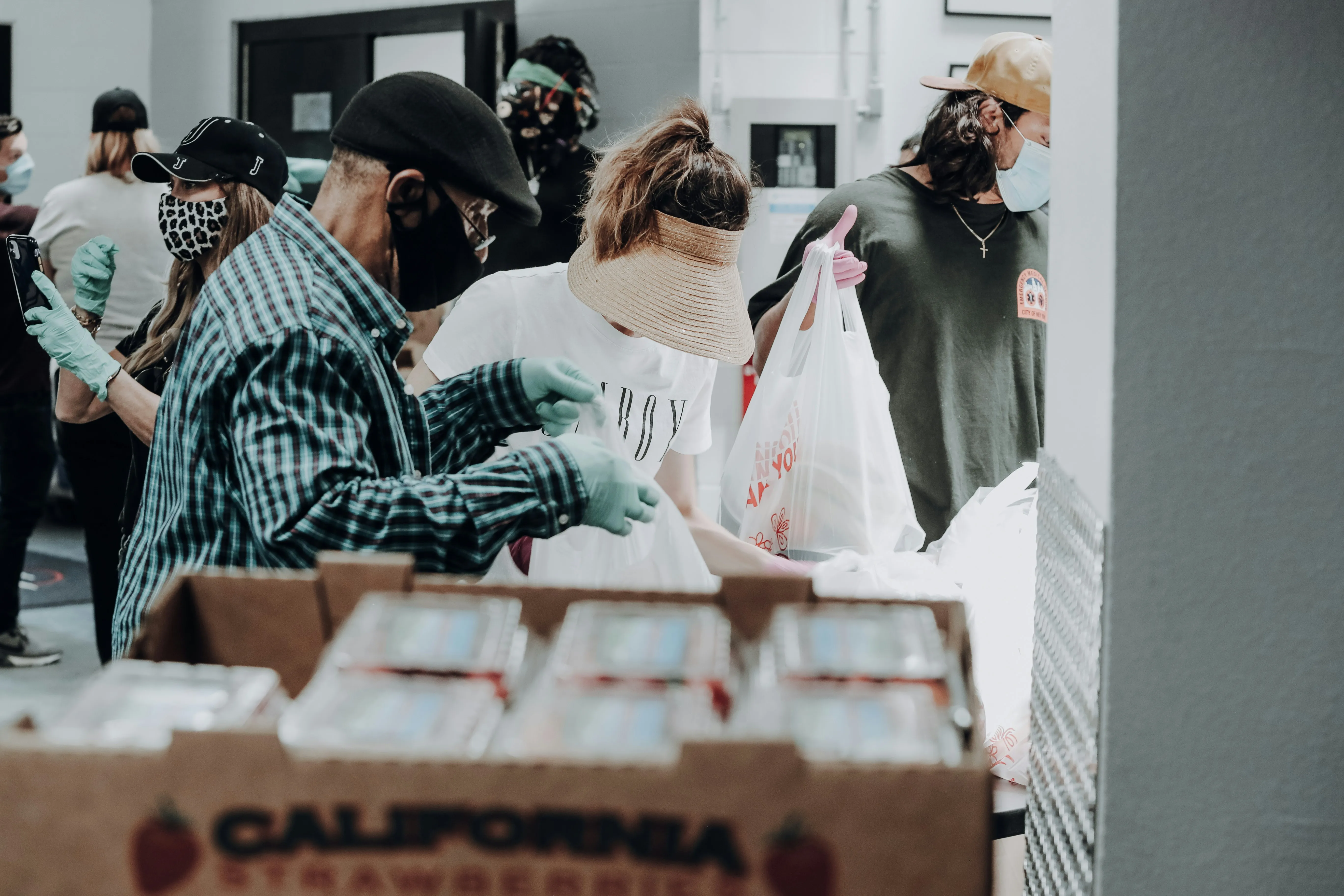 People wearing masks and gloves packing food supplies inside a community food bank or shelter.