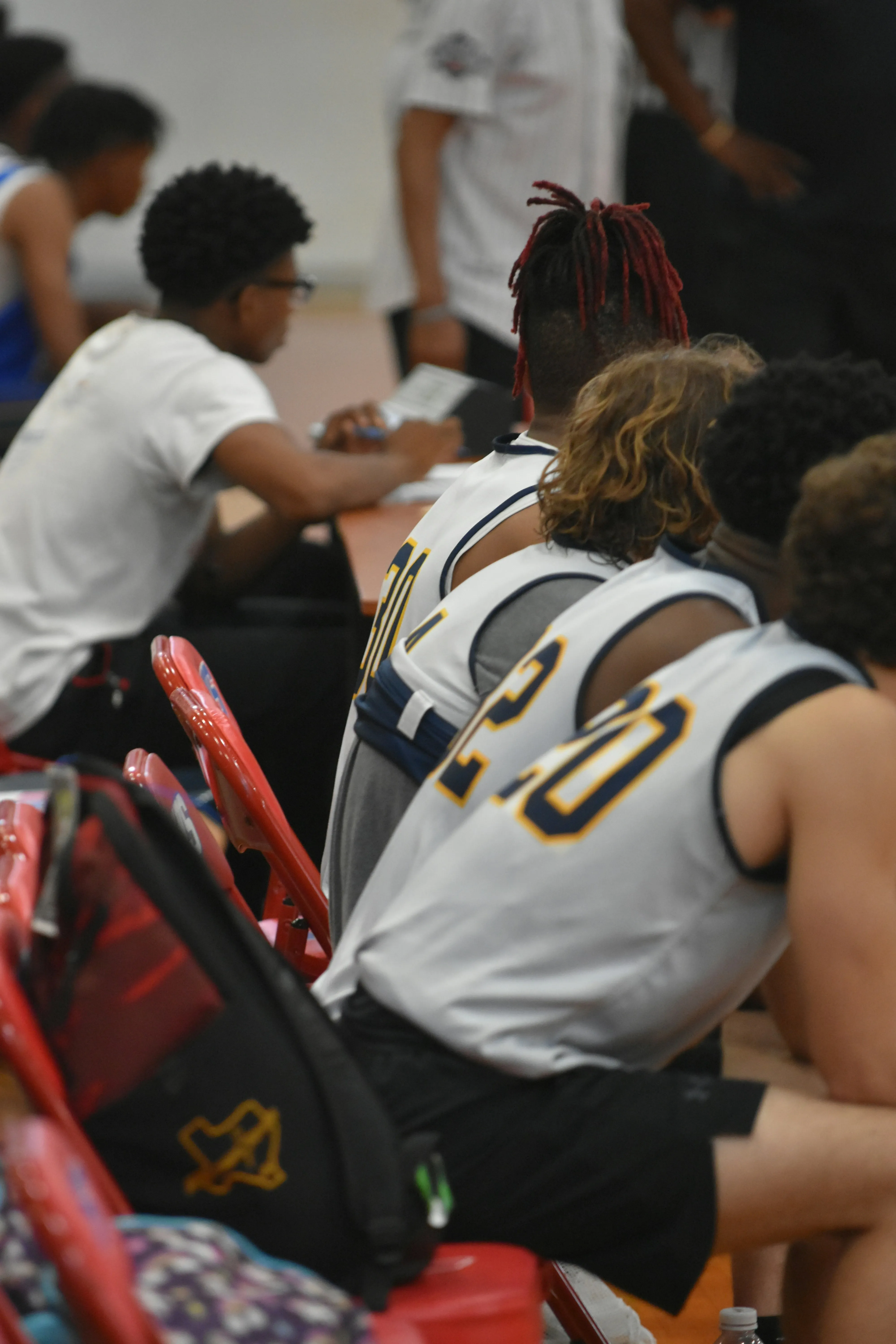 Basketball players sitting side by side on red chairs, watching the game.