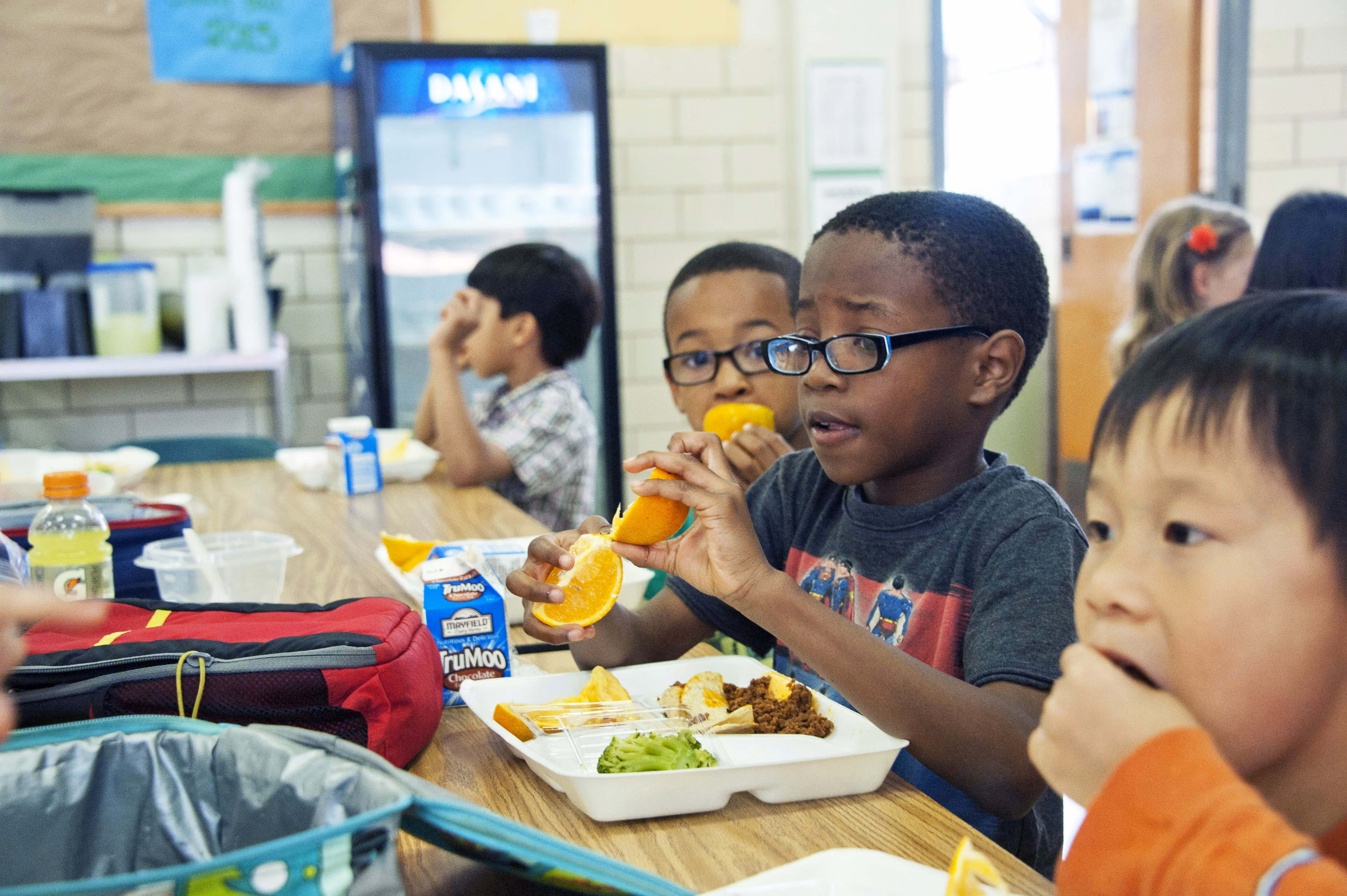 Young boys sitting at a cafeteria table eating lunch, including oranges and milk cartons.