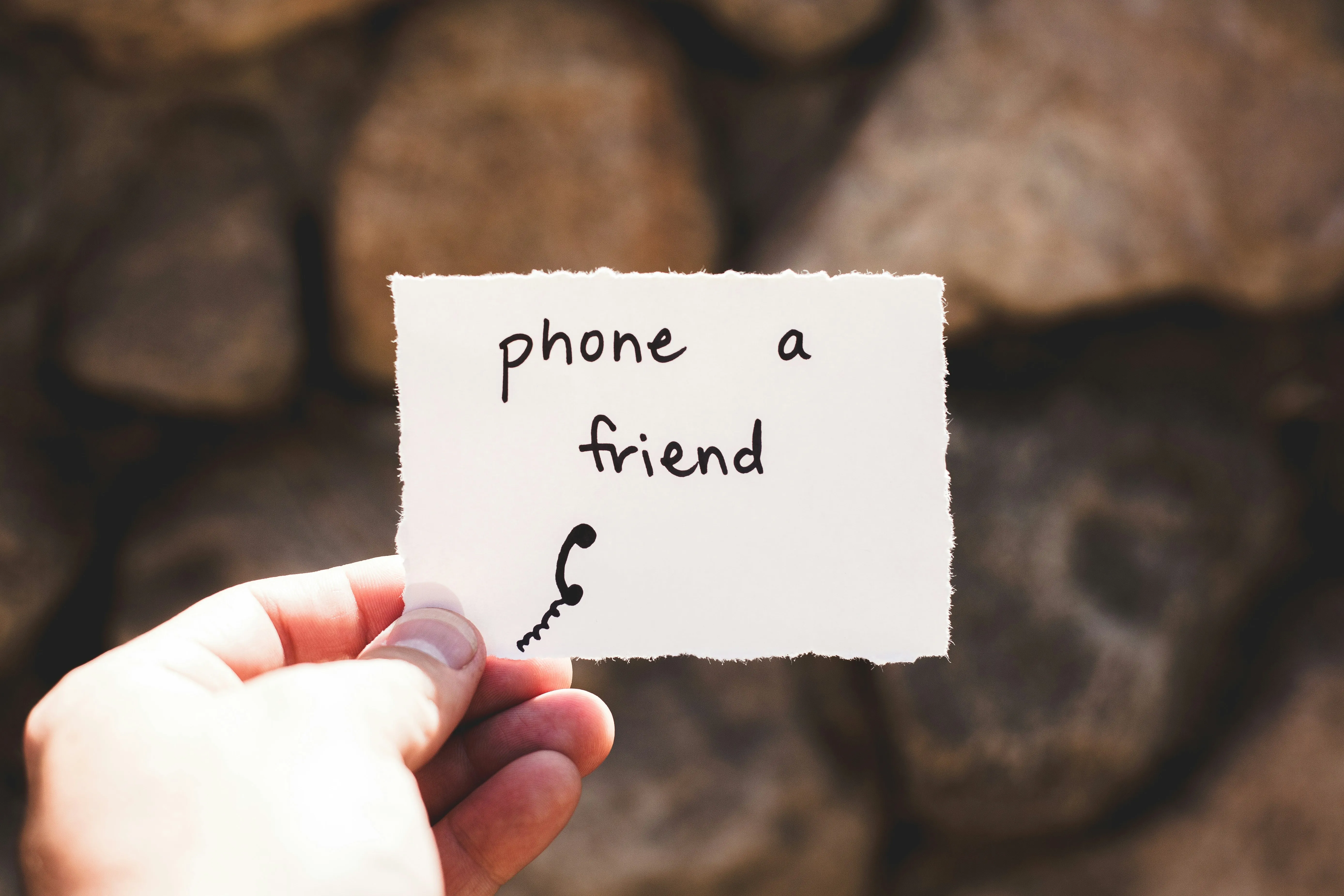 Hand holding a torn paper with 'phone a friend' and a phone icon on it.