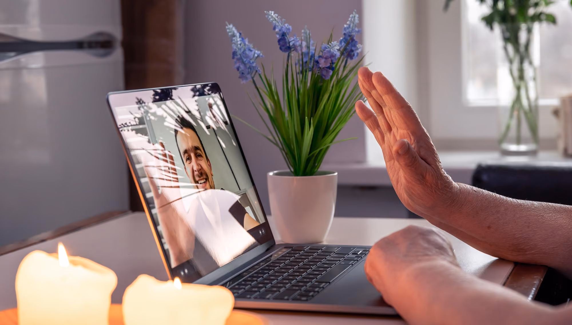 Person with raised hand on video call waving to a smiling man on a laptop screen.