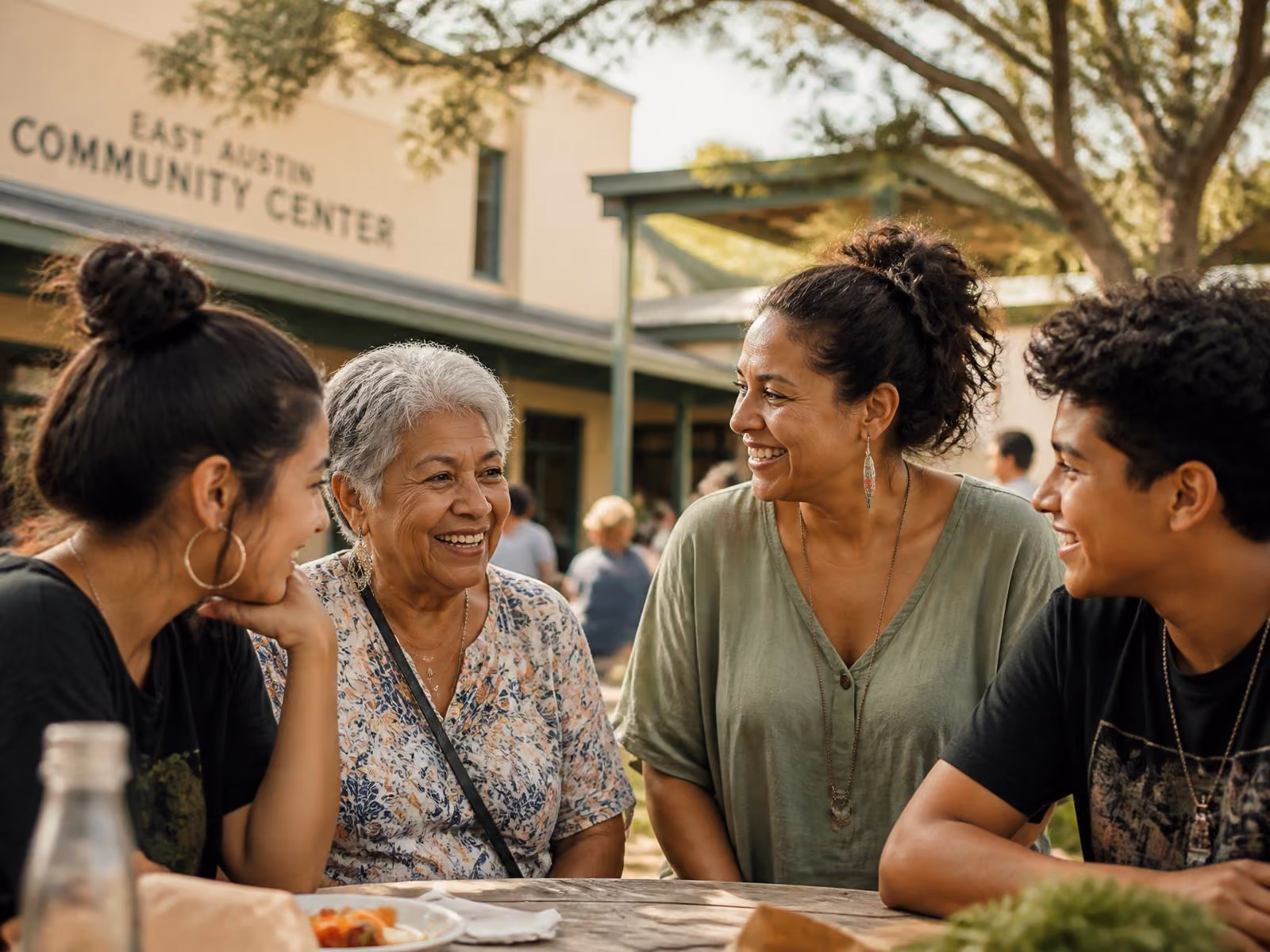 Four people smiling and chatting at an outdoor table near East Austin Community Center.
