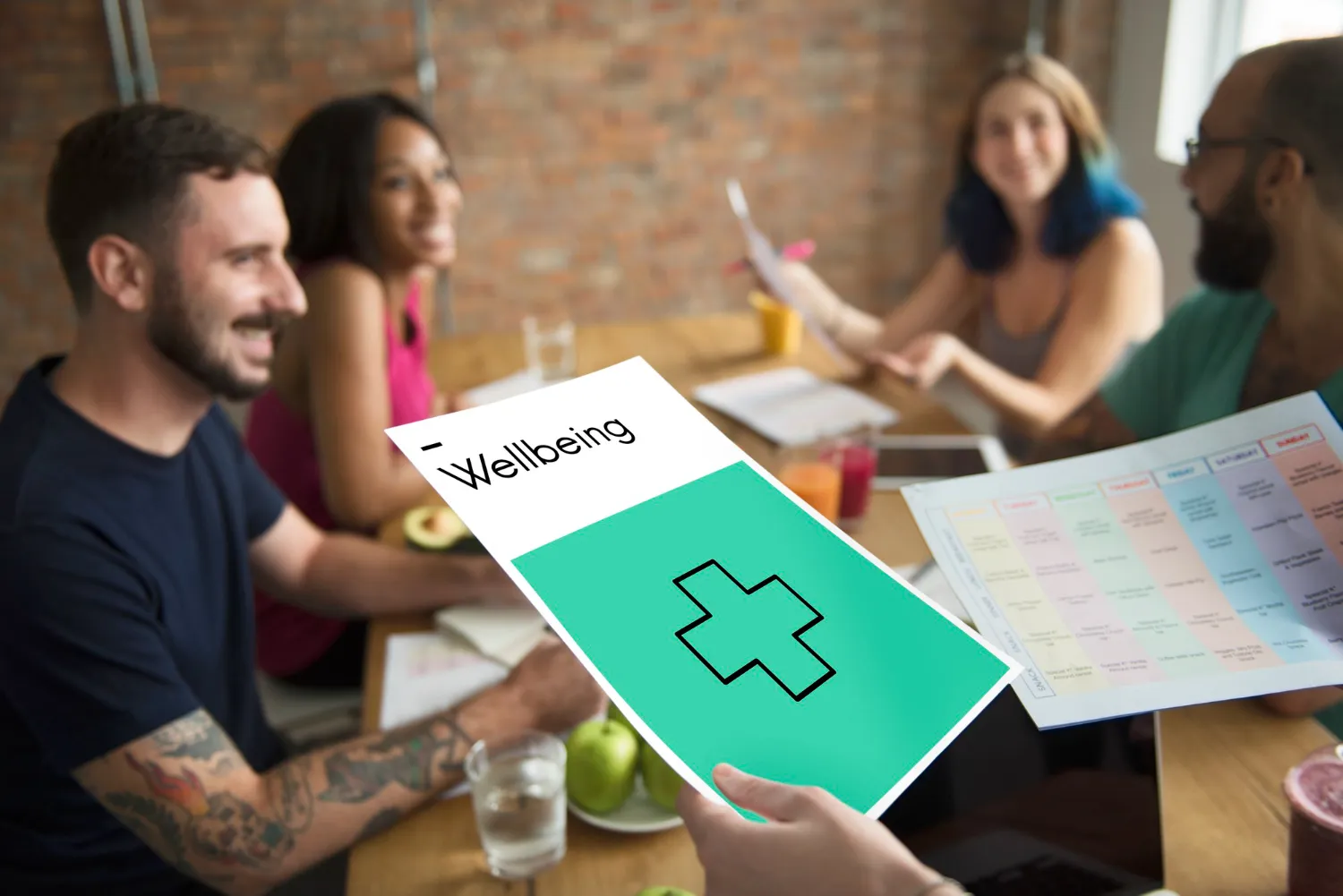 Group of four smiling people holding wellness and meal planning papers at a table.