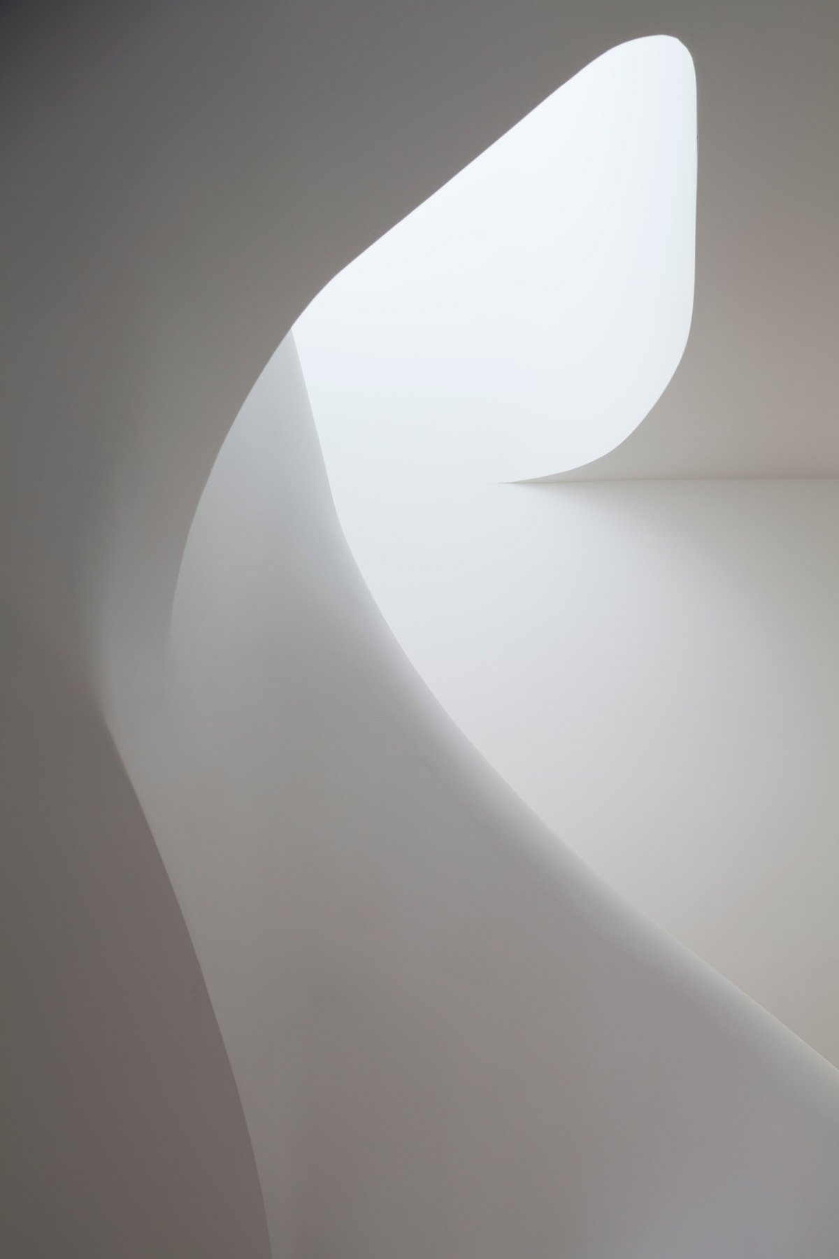 Curved white stair enclosure lit from the rooflight above
