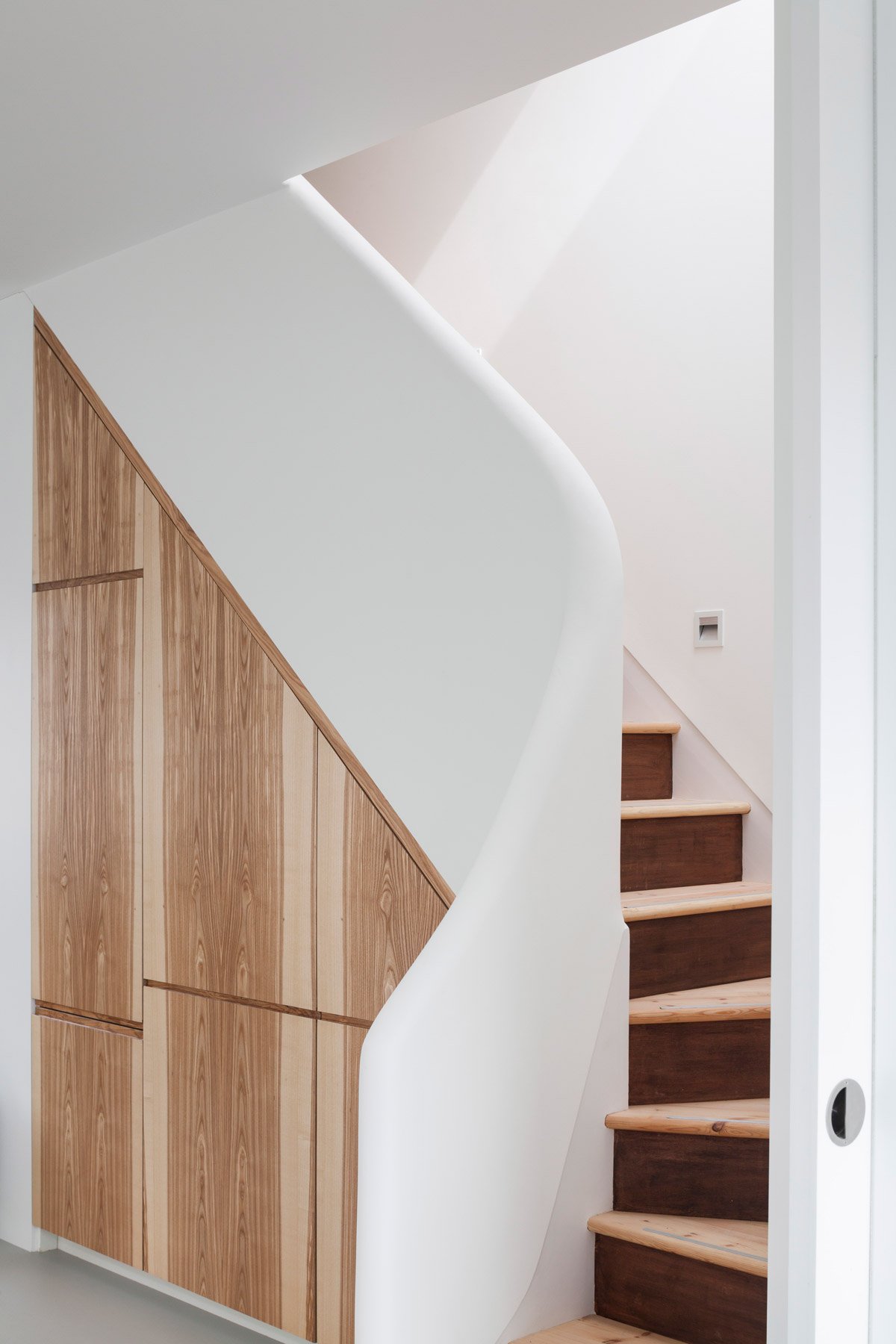Timber stair rising past fitted oak cupboards, with a sculpted white balustrade