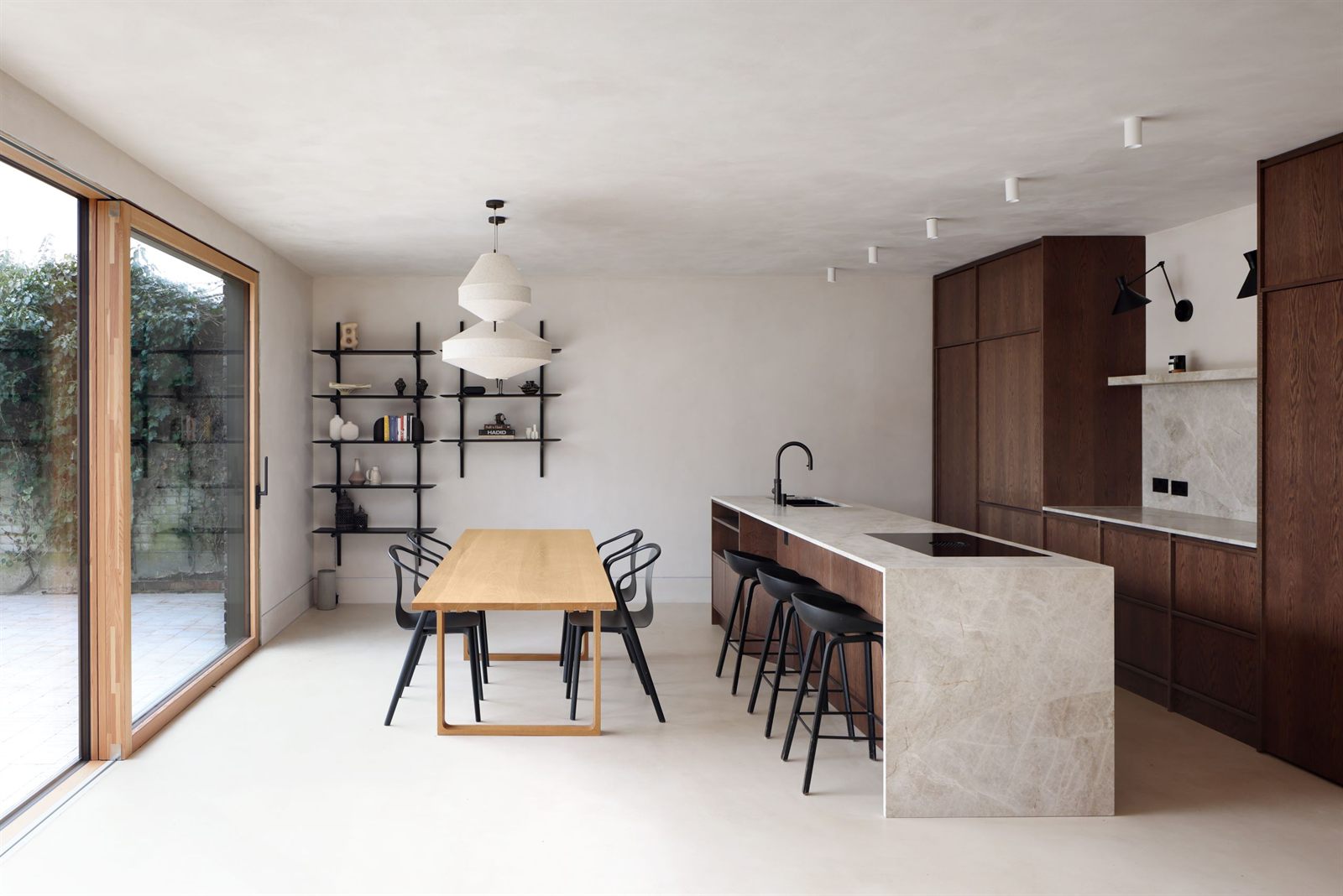 Dining table and black shelving beside the sliding glazing, with the kitchen opposite