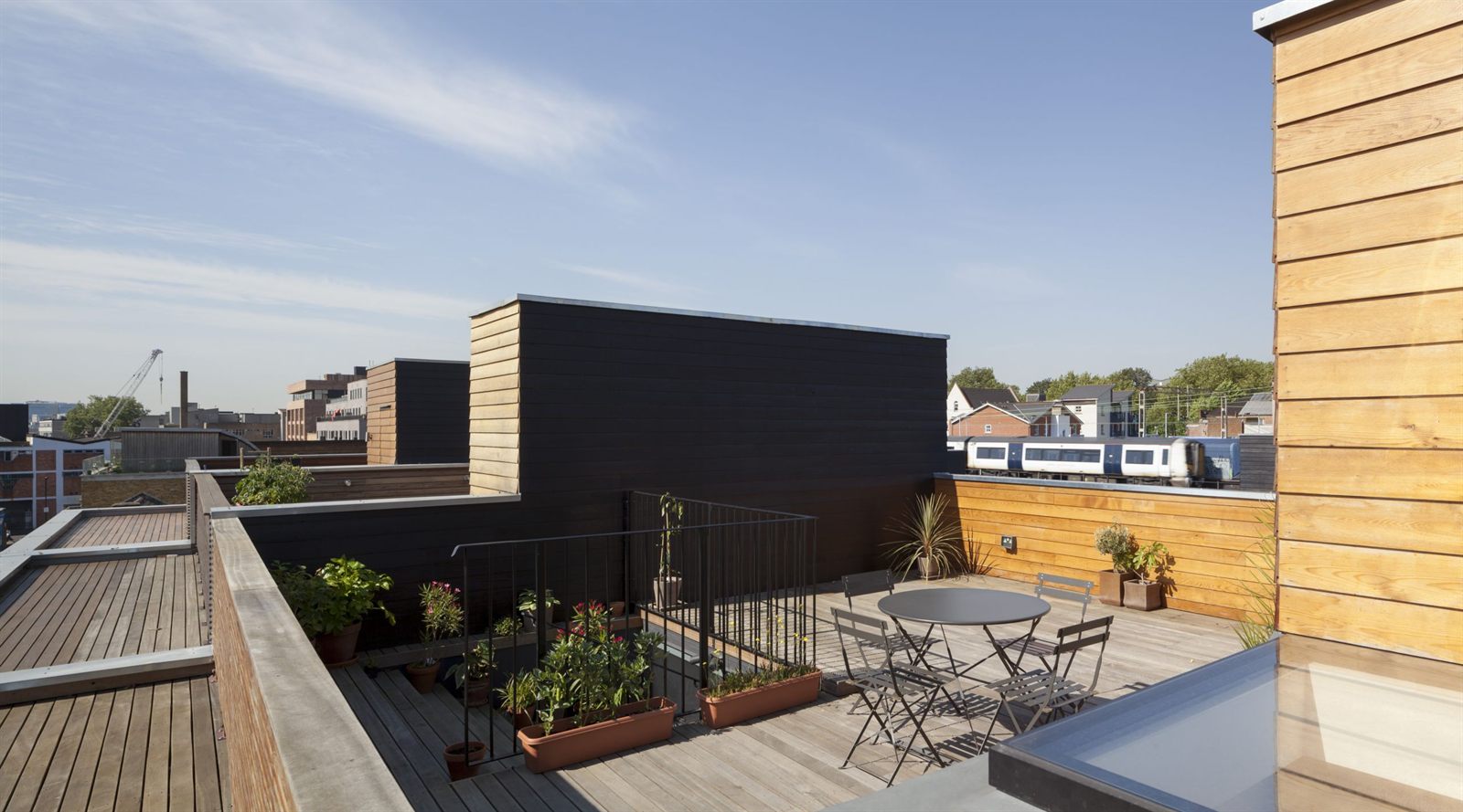 Roof terrace with timber decking and planters, looking out over the railway and rooftops