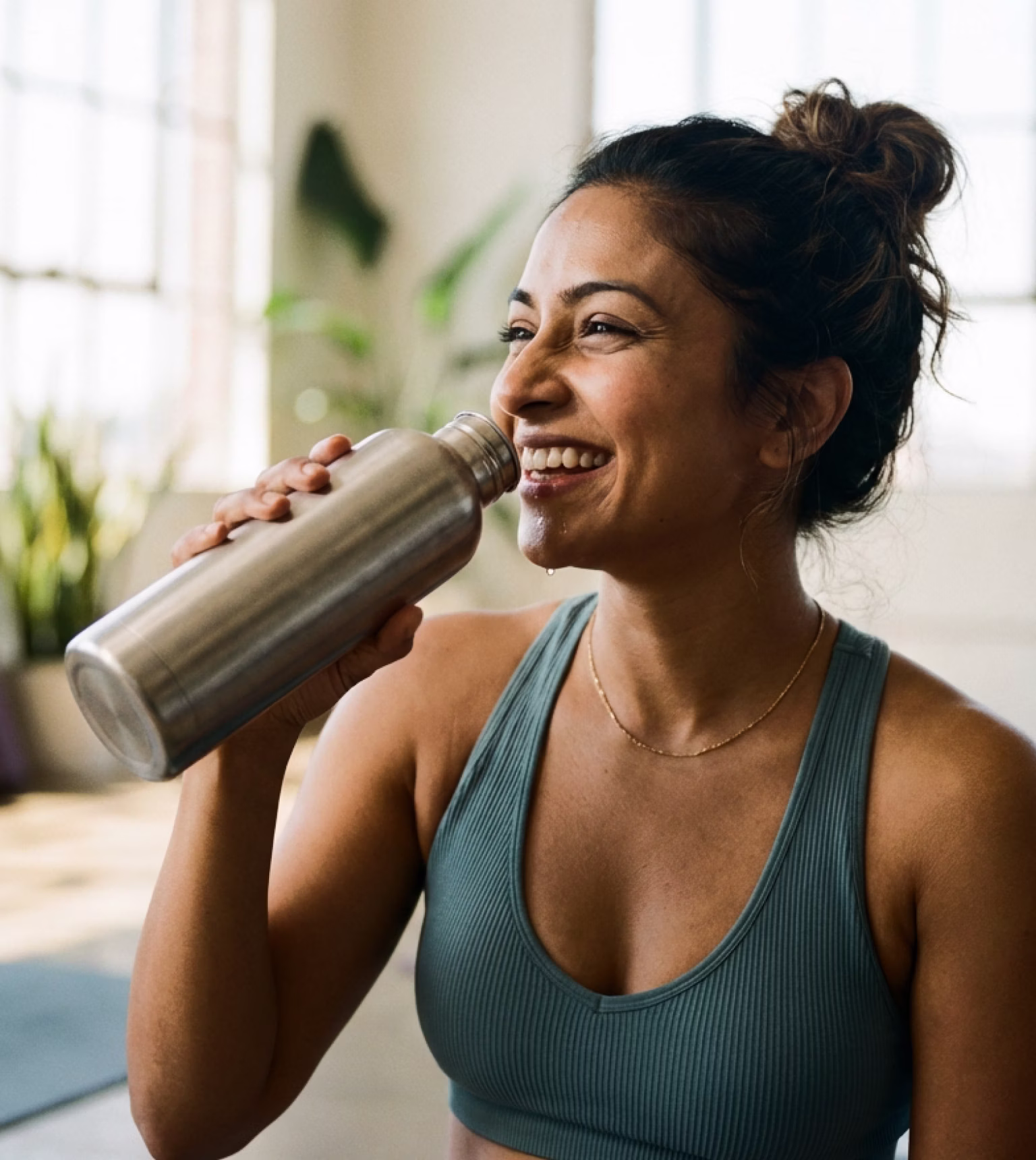 Smiling woman drinking water from a bottle after yoga practice