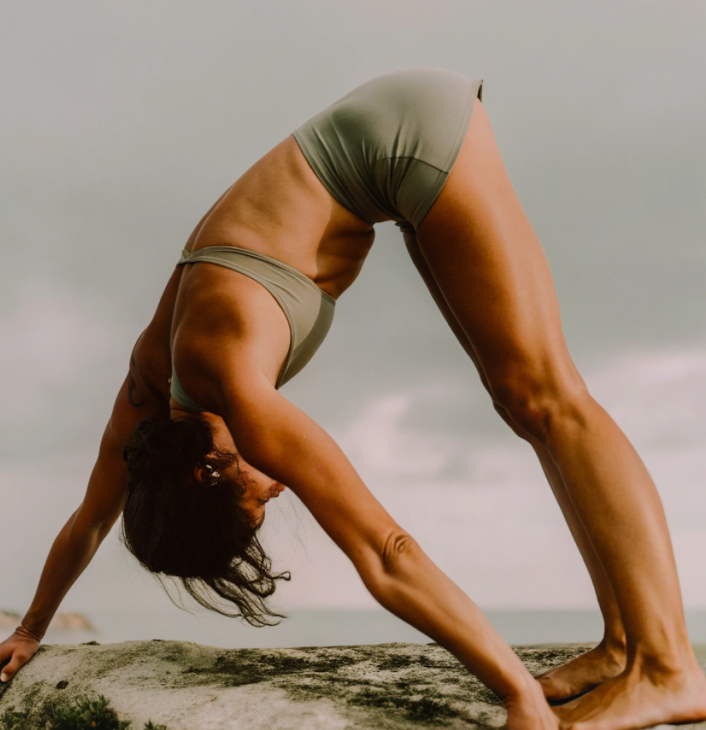 Woman in backbend yoga pose on a rock by the sea