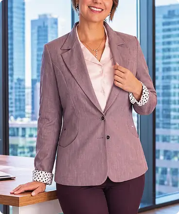 Uniforme corporativo para mujer con saco color malva texturizado y blusa blanca en entorno de oficina.