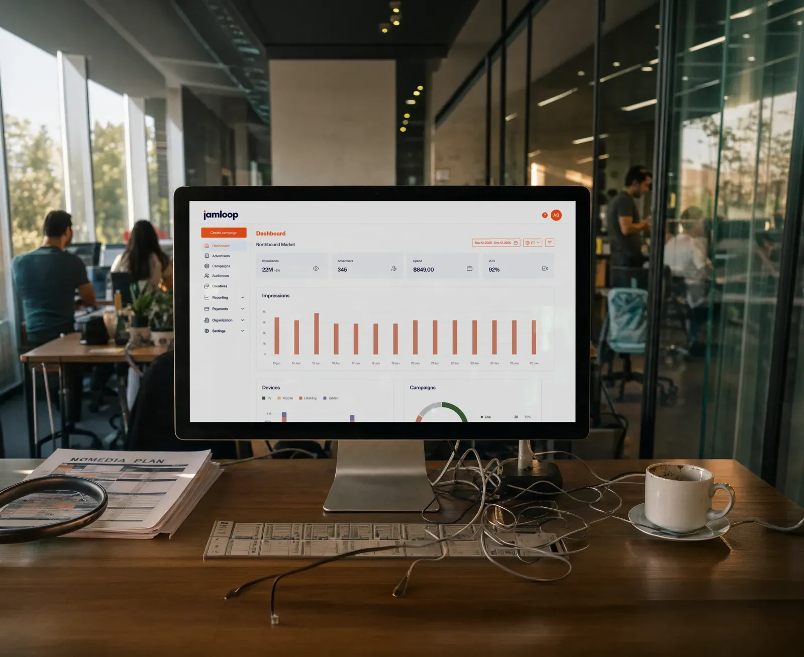 Computer monitor on desk displays a marketing dashboard with charts, papers, and coffee cup nearby.