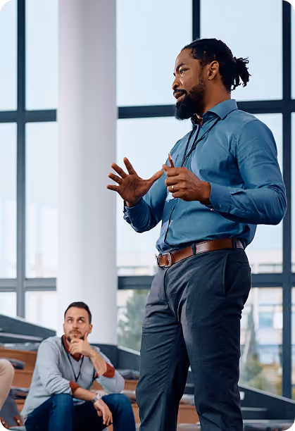 Businessman speaking and gesturing with an audience member listening thoughtfully behind him.
