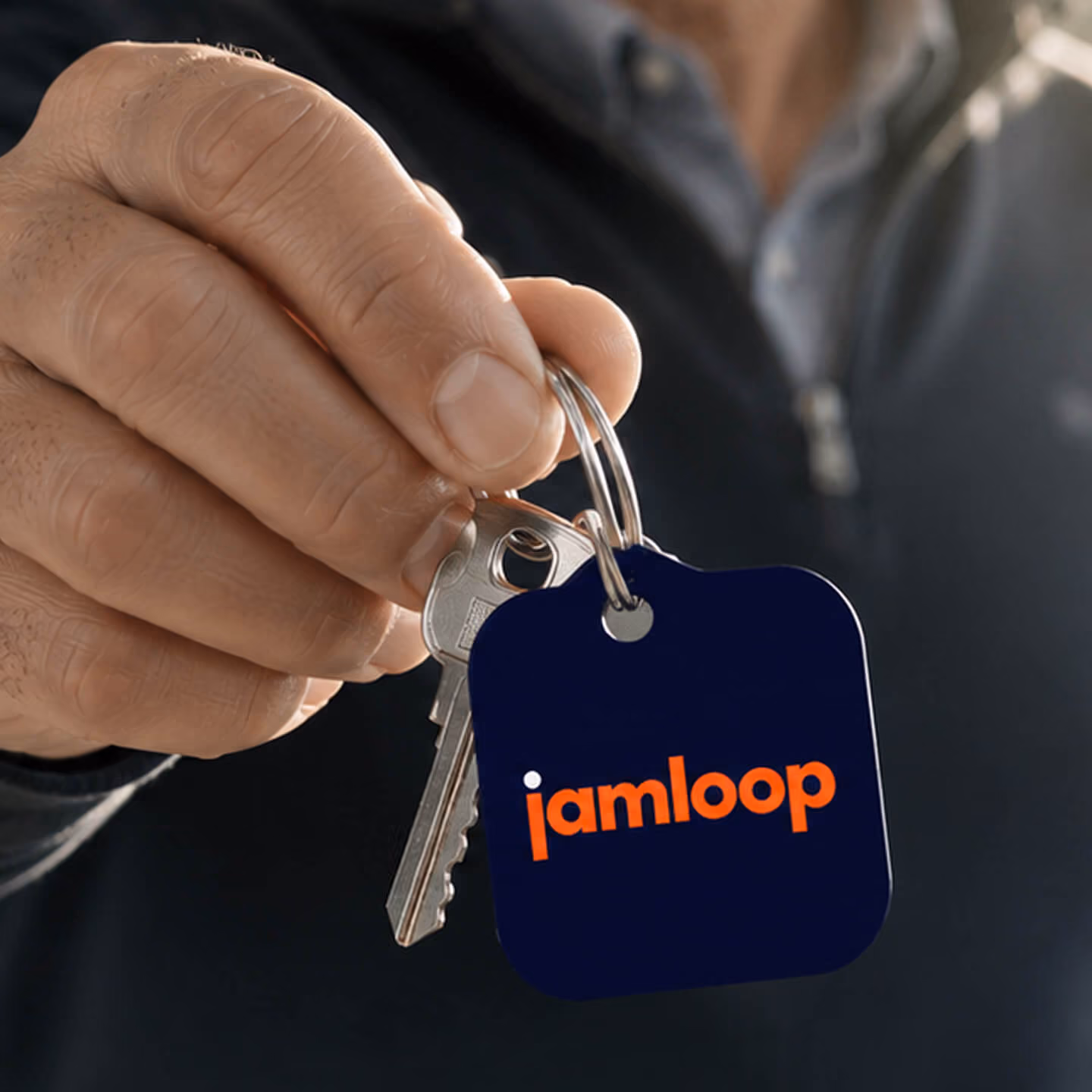 A hand holds a set of keys with a dark blue keychain that has the word 'jamloop' written in orange letters.