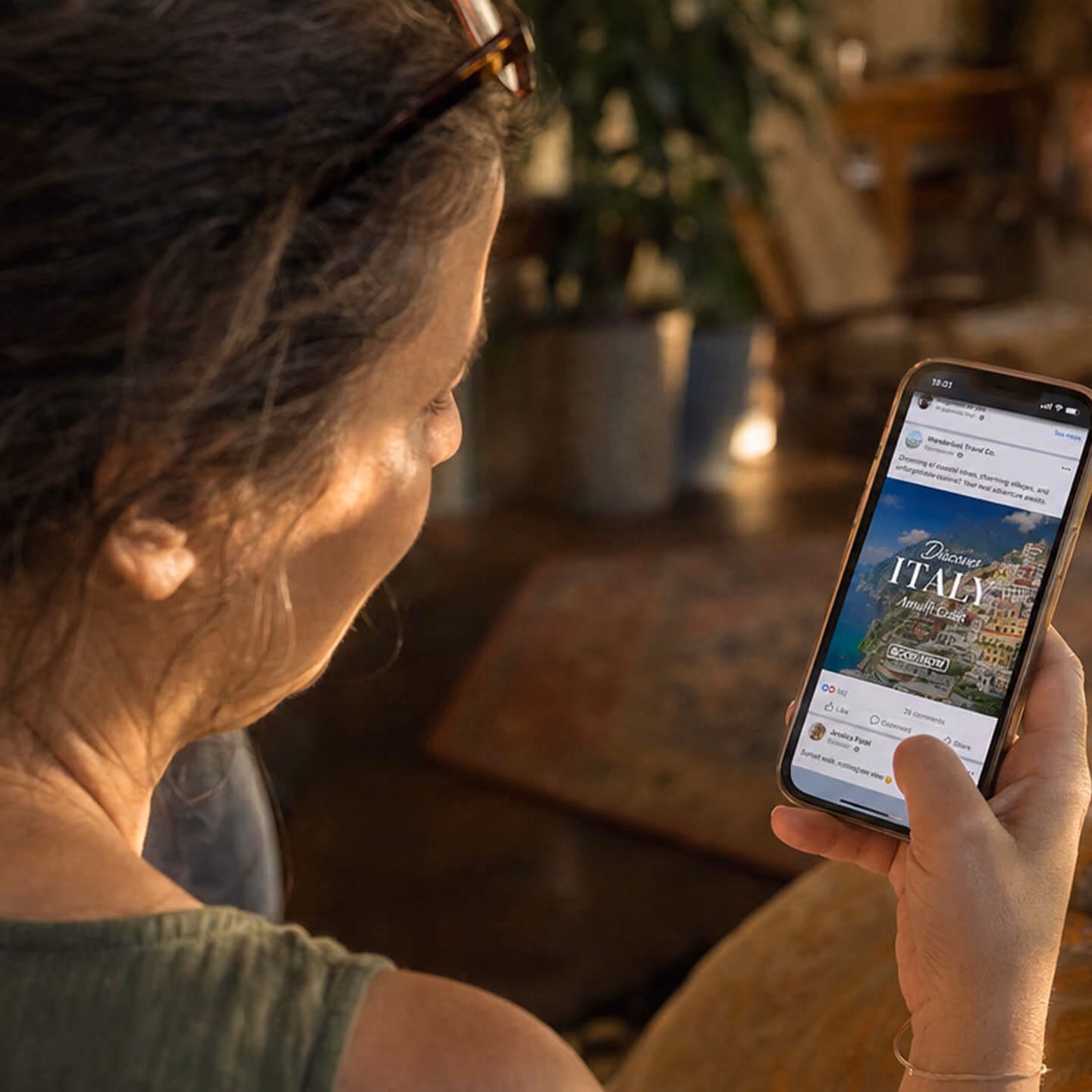Woman with glasses on her head looking at a smartphone displaying a travel ad for Italy, Amalfi Coast.
