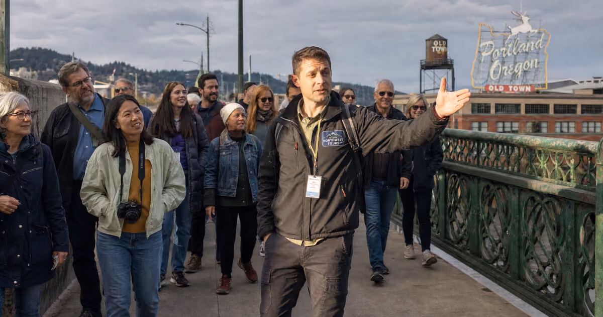 Tour guide leading a group across a bridge in Portland's Old Town, with the Portland Oregon sign in the background