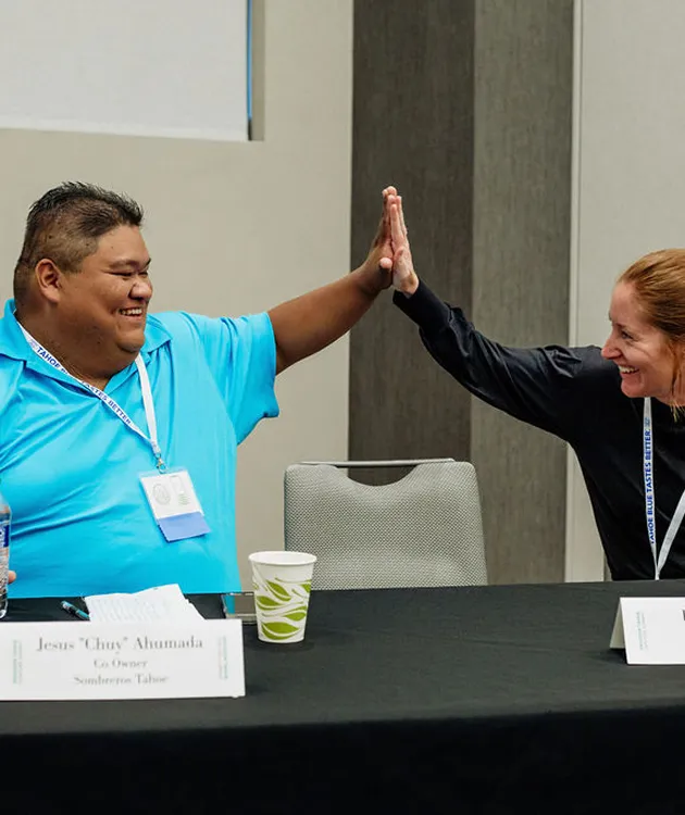 Two people smiling and giving a high five over a table with name tags and cups.