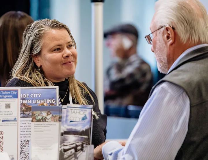 A woman talks to an older man across a booth with brochures about Tahoe City.