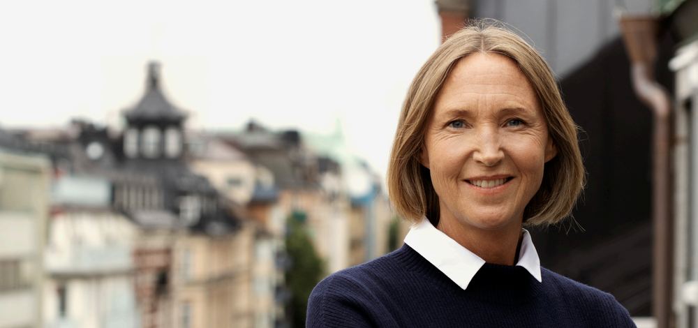 Porträtt av en leende kvinna framför stadsbebyggelse