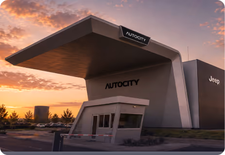 Modern AUTOCITY building with Jeep branding at sunset and a guardhouse in front.