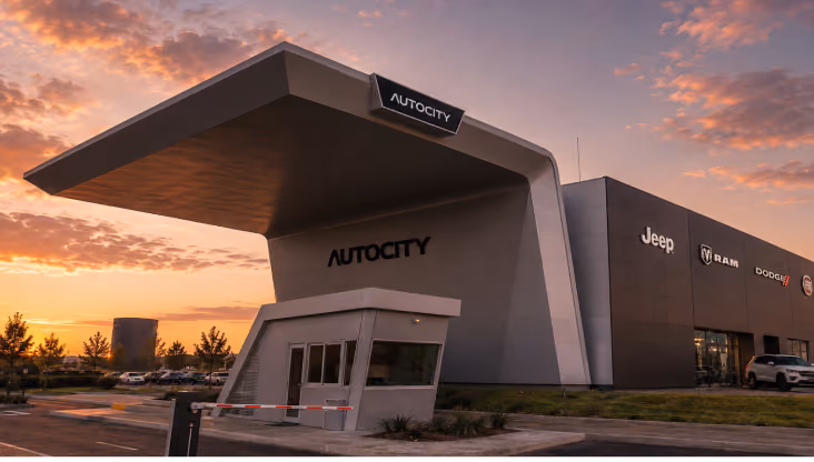 Modern AUTOCITY building with Jeep branding at sunset and a guardhouse in front.