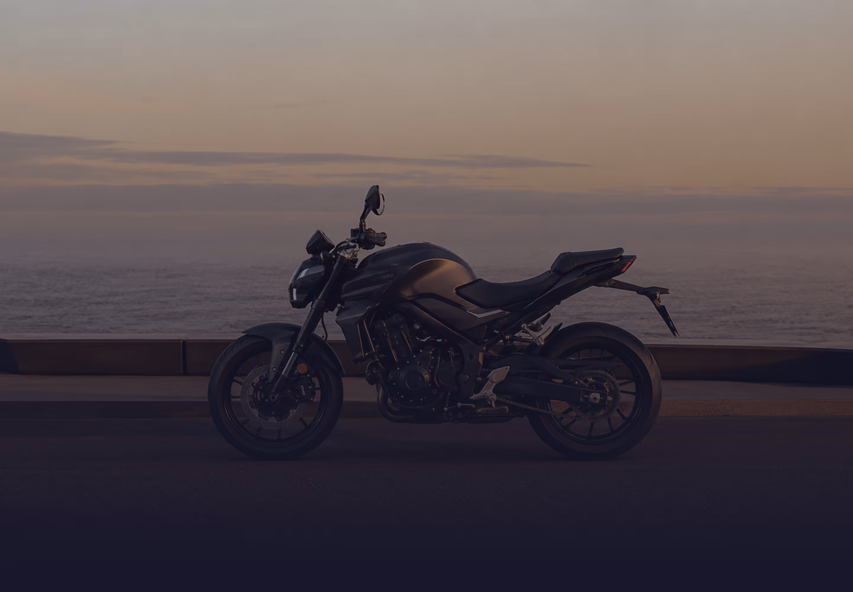 Motocicleta negra estacionada junto al mar durante el atardecer.