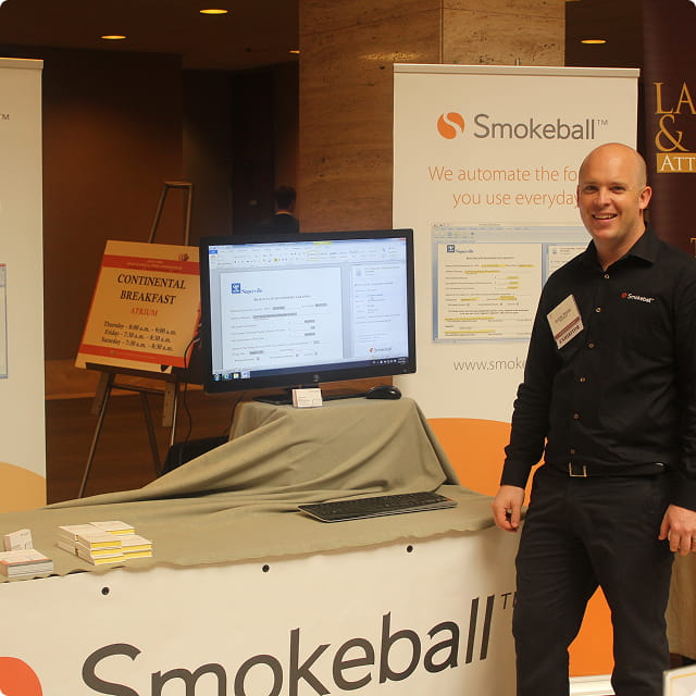 Man standing at a Smokeball booth with computer monitor displaying legal software interface.