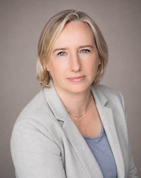 Professional headshot of a woman with blonde hair wearing a light gray blazer