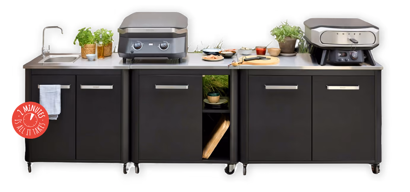 Udendørs køkken med vask, planter, to griller, madvarer og køkkenskabe på hjul.