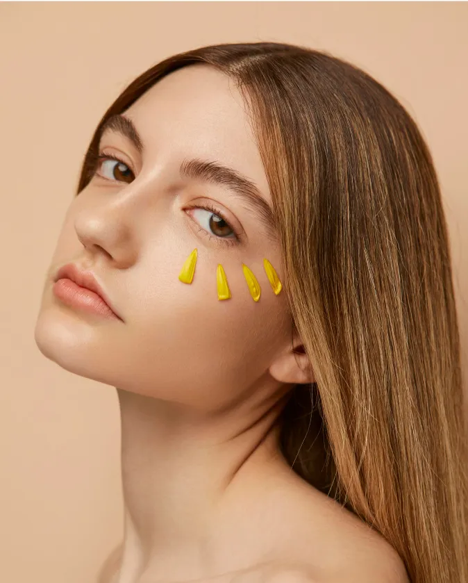 Young woman with long straight brown hair tilting her head sideways, with four yellow flower petals arranged under her right eye.
