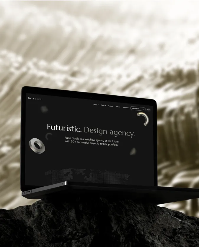 Black laptop displaying a website for Futur Studio, a futuristic design agency, set on a textured dark rock with a blurred abstract background.