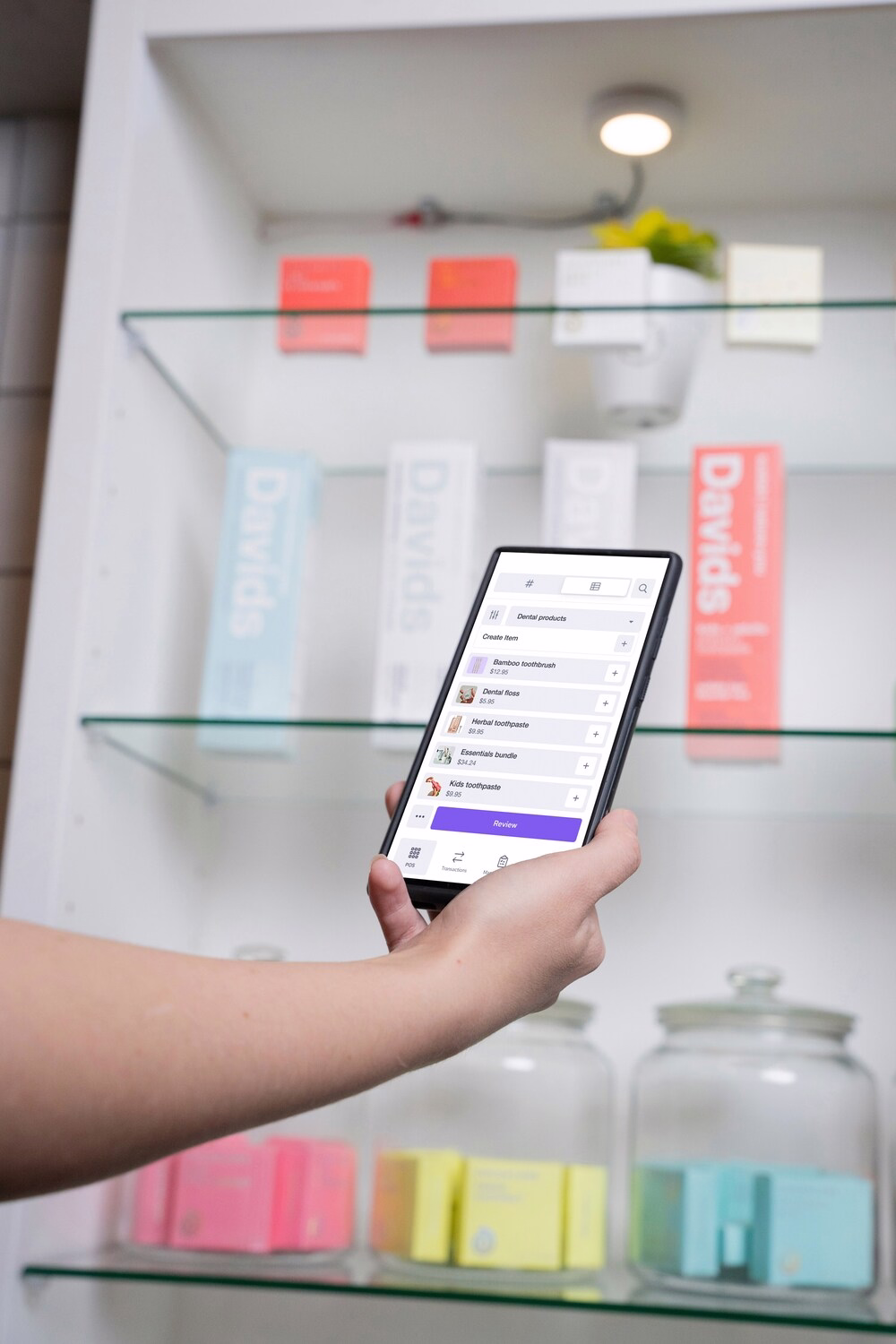 Person holding smartphone showing dental product list and prices in front of store shelves.