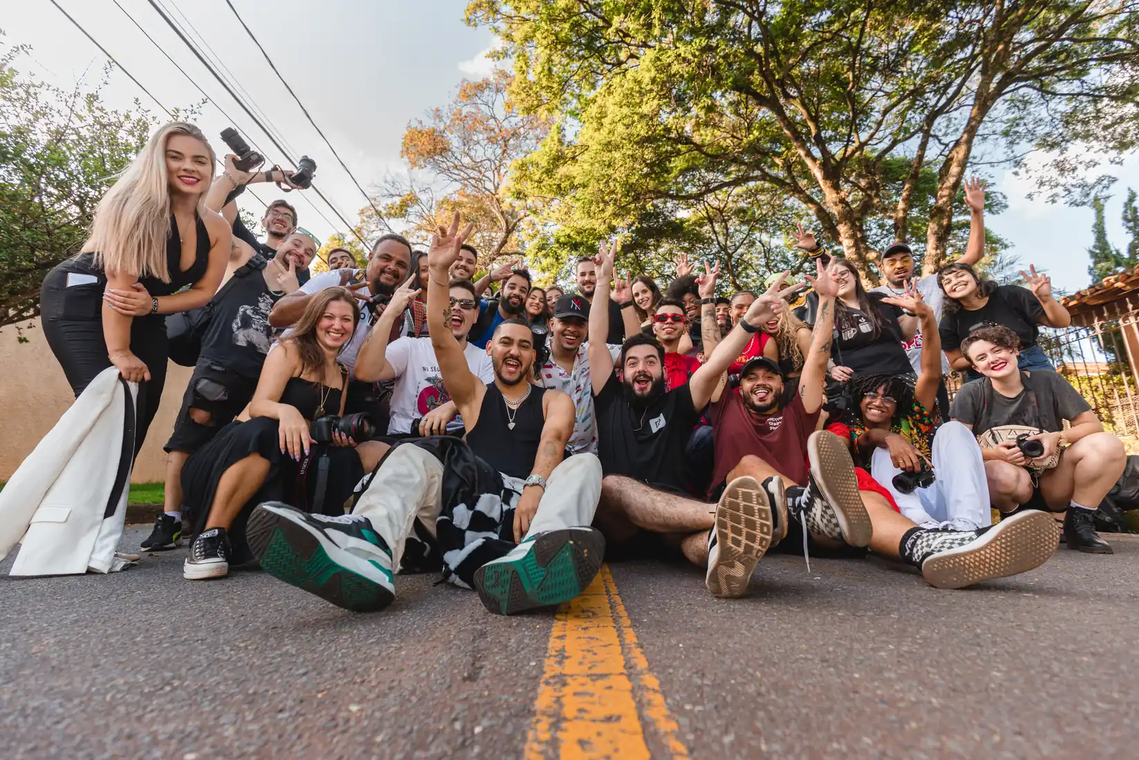 Large group of creators sitting on a street and cheering at the camera