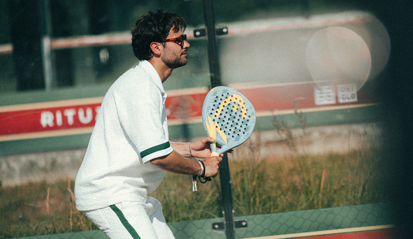 Player in white kit serving with a padel racket on an outdoor court
