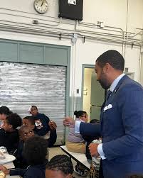 Male speaker in suit addressing students in a classroom