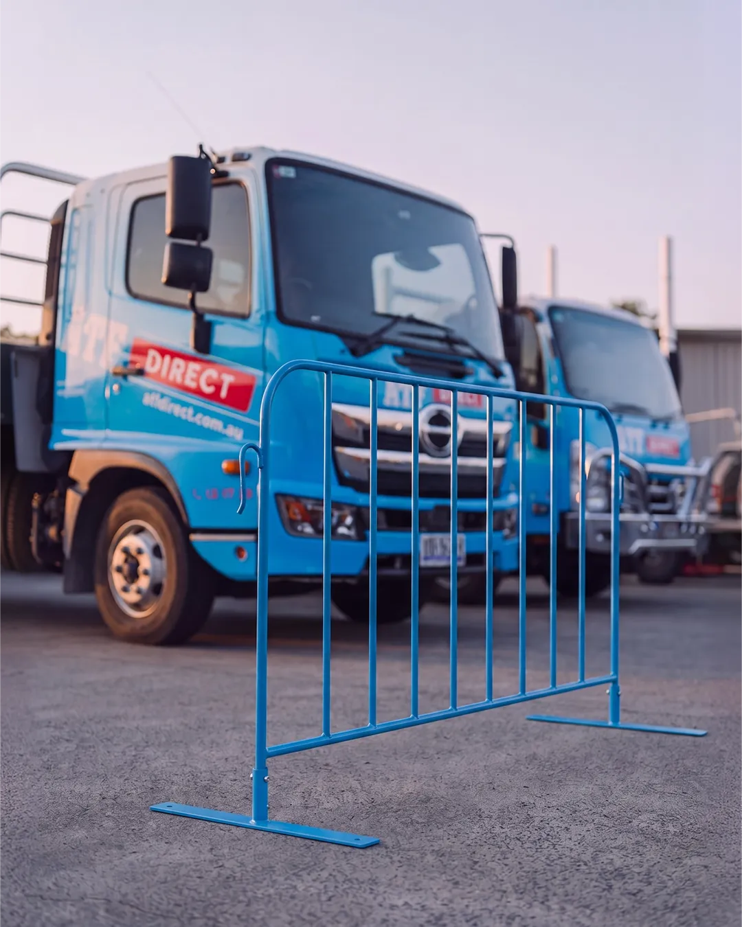 Blue metal barricade with two blue trucks parked behind it on a concrete surface.