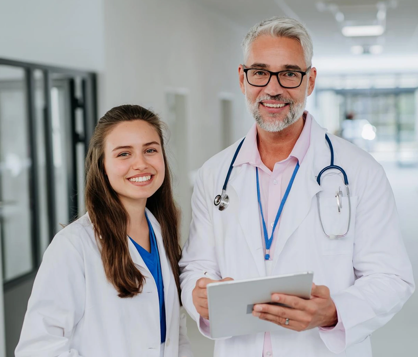 Smiling female doctor in white coat holding a black clipboard with stethoscope around her neck.