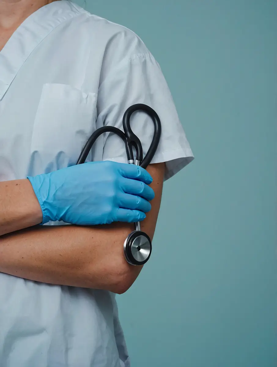 Healthcare professional in a white coat and blue gloves holding a black stethoscope.