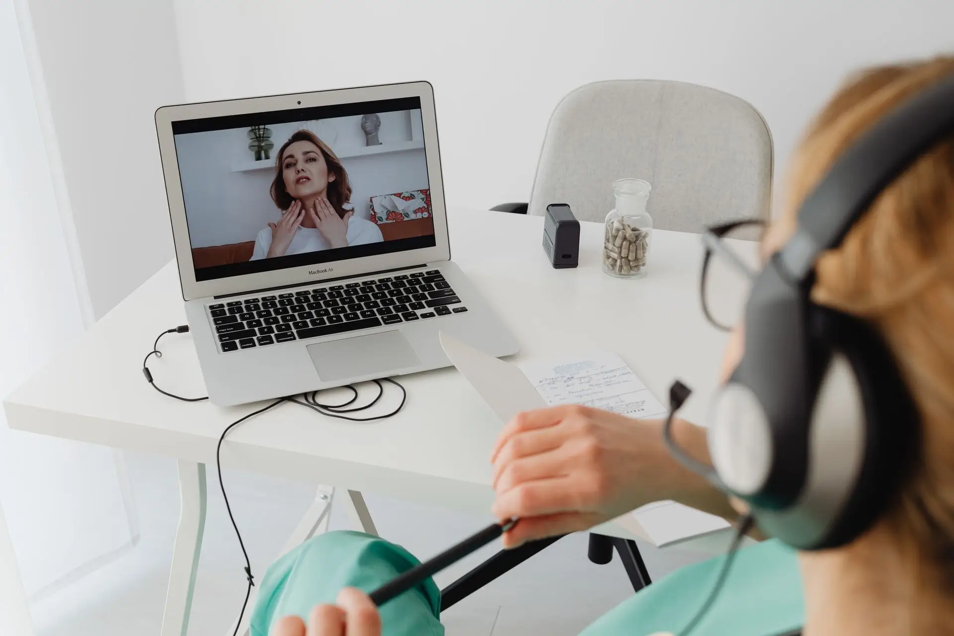 Person with headset doing a video call with another woman showing her neck on a laptop screen.