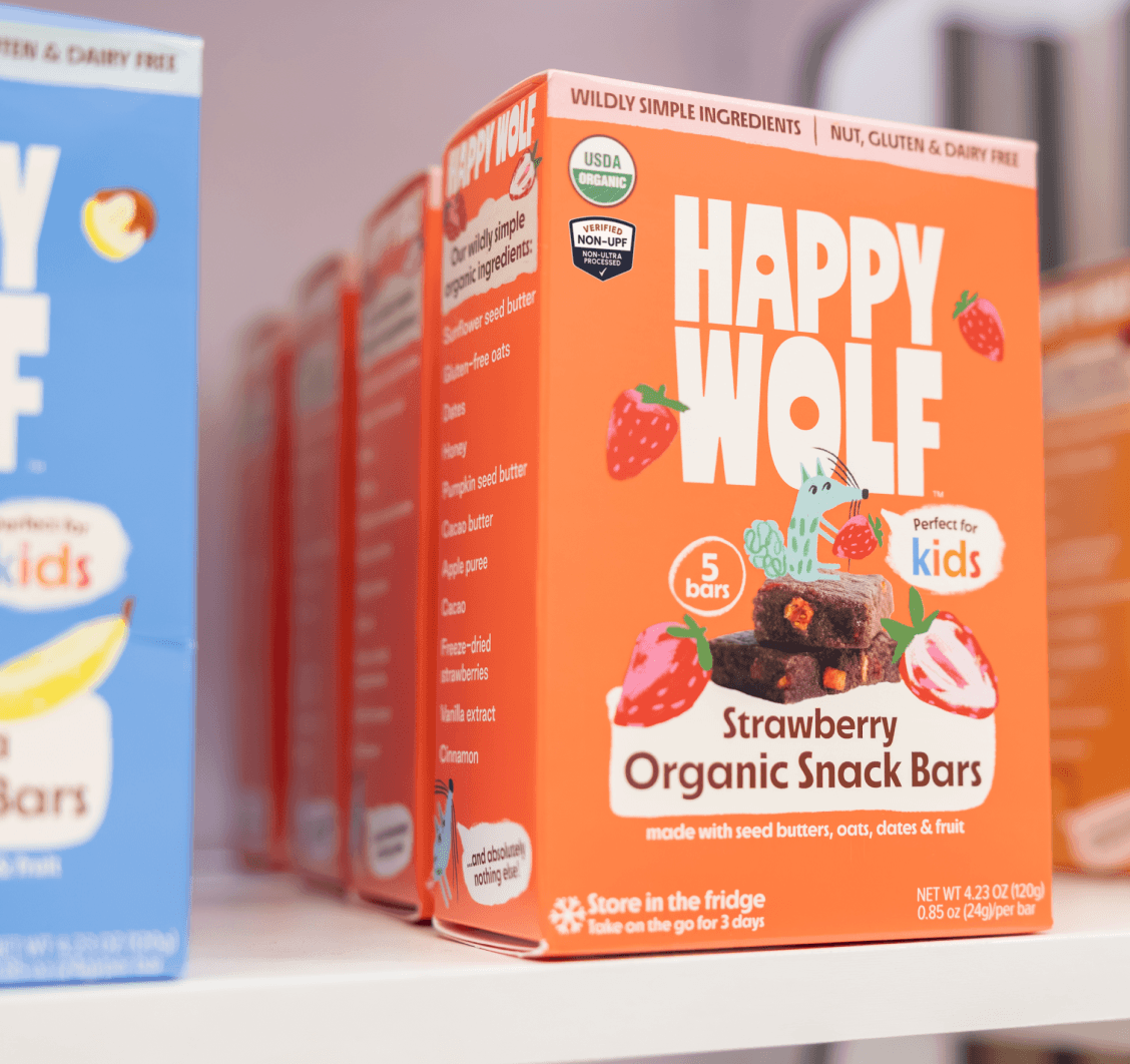 Boxes of Happy Wolf Strawberry Organic Snack Bars on a shelf, made with oats and fruit with the Non-UPF Shield.